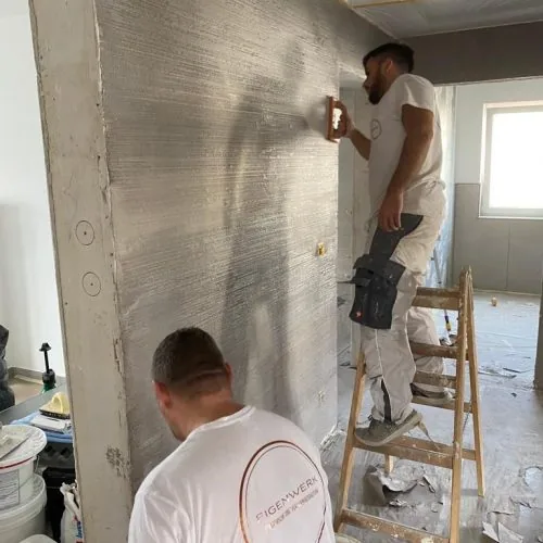 Hand zieht mit der Kelle eine Kalkspachtelschicht über eine Wandfläche