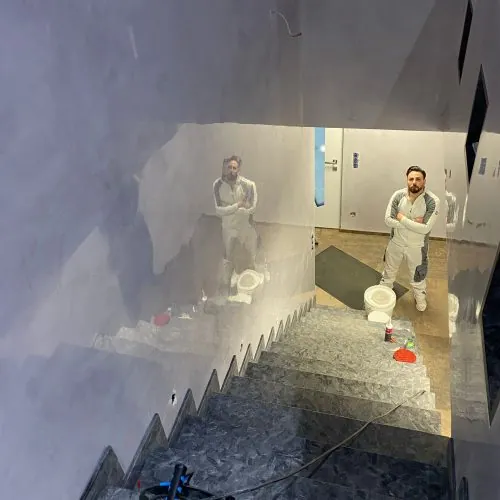 Treppenhaus während der Ausführung: zwei Handwerker vor frisch gespachtelten Wandflächen