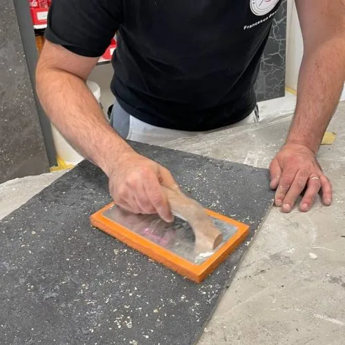 Zwei Hände ziehen mit der Glättkelle eine frische Spachtelmasse über eine Musterplatte