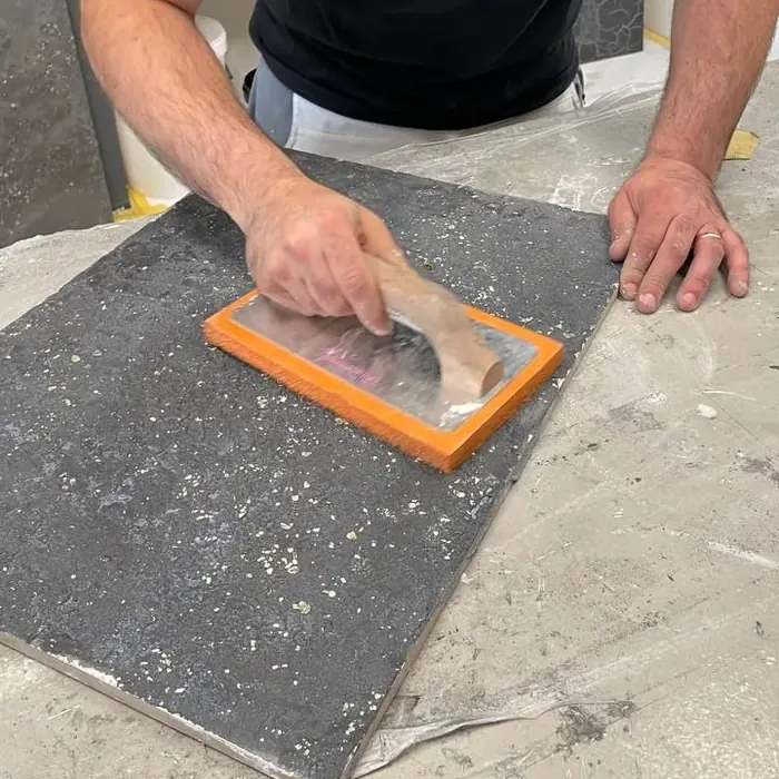 Mitarbeiter von Eigenwerk zieht mit der Glättkelle eine dunkle Spachtelmasse über eine Musterplatte