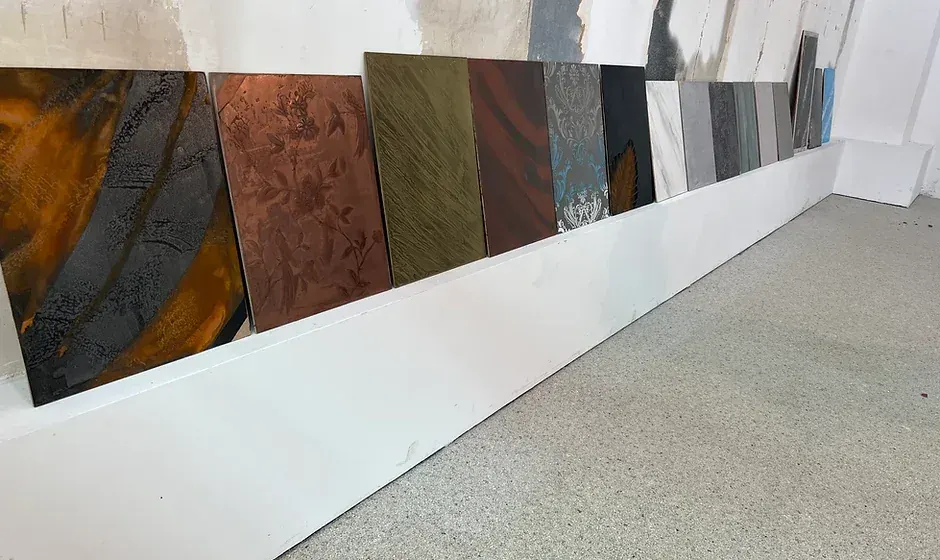 Reihe fertiger Musterplatten in Kupfer, Rost, Grau und Weiß, aufgestellt an einer Wand