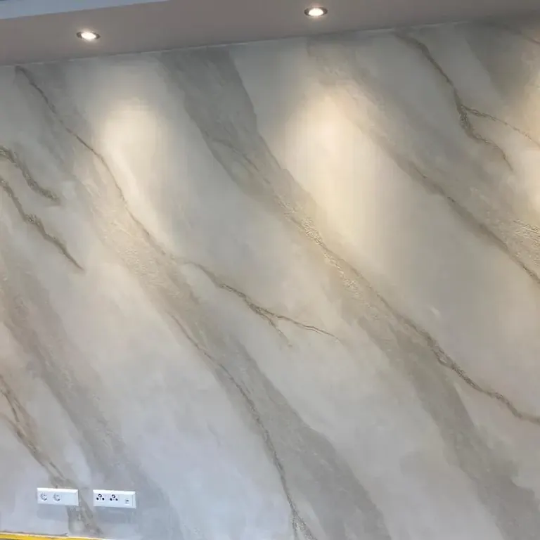 Große Wandfläche in heller Marmoroptik mit grauen Adern, von Deckenstrahlern angeleuchtet