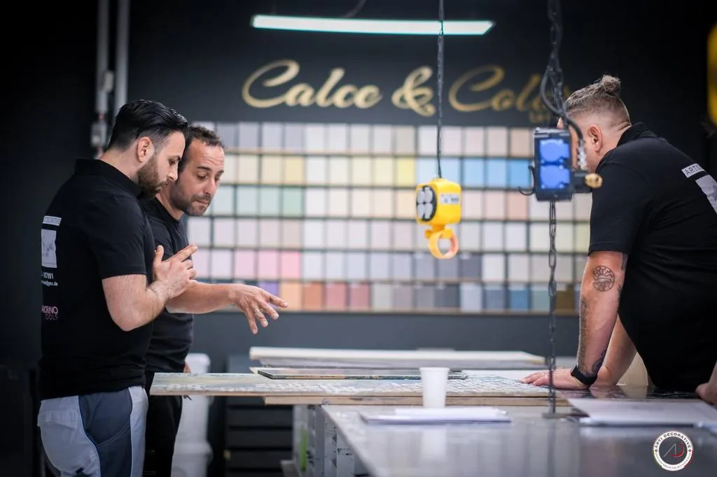 Drei Mitarbeiter an der Farbmusterwand «Calce & Colore», Musterplatte auf dem Tresen
