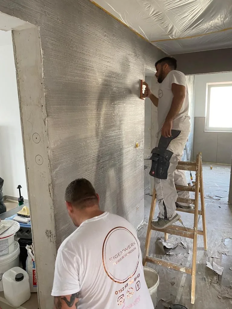 Zwei Handwerker spachteln von der Leiter aus eine hohe Wandfläche