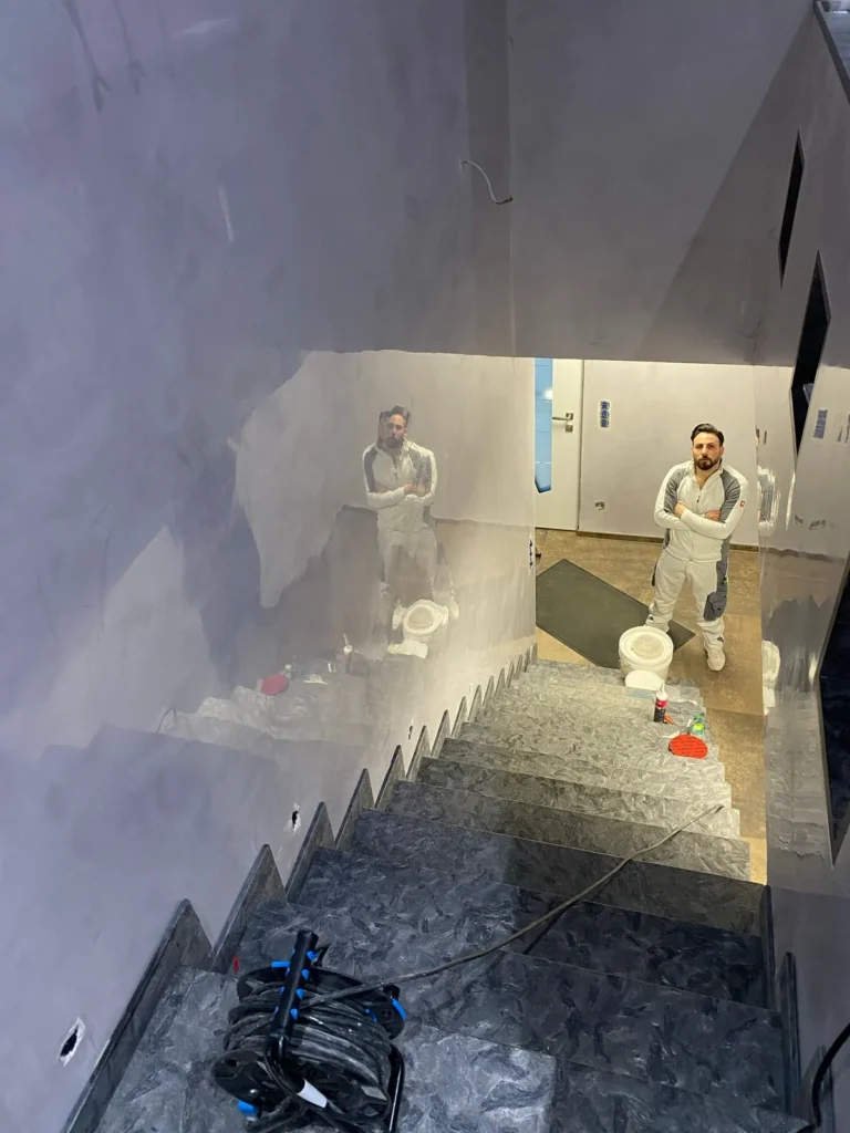 Treppenhaus während der Ausführung: Handwerker vor frisch gespachtelten Wänden, Treppe in dunklem Naturstein