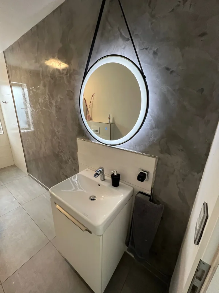 Badezimmer mit Doppelwaschtisch und ovalem Spiegel vor gespachtelter Wand